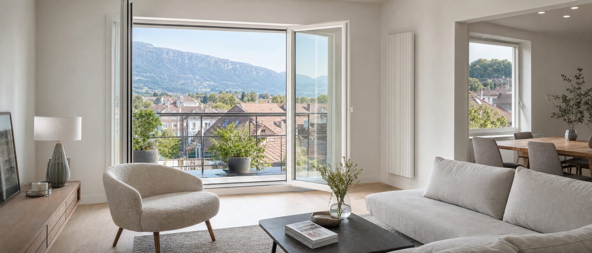Salon lumineux ouvert sur un balcon, toits d'Annemasse en fond